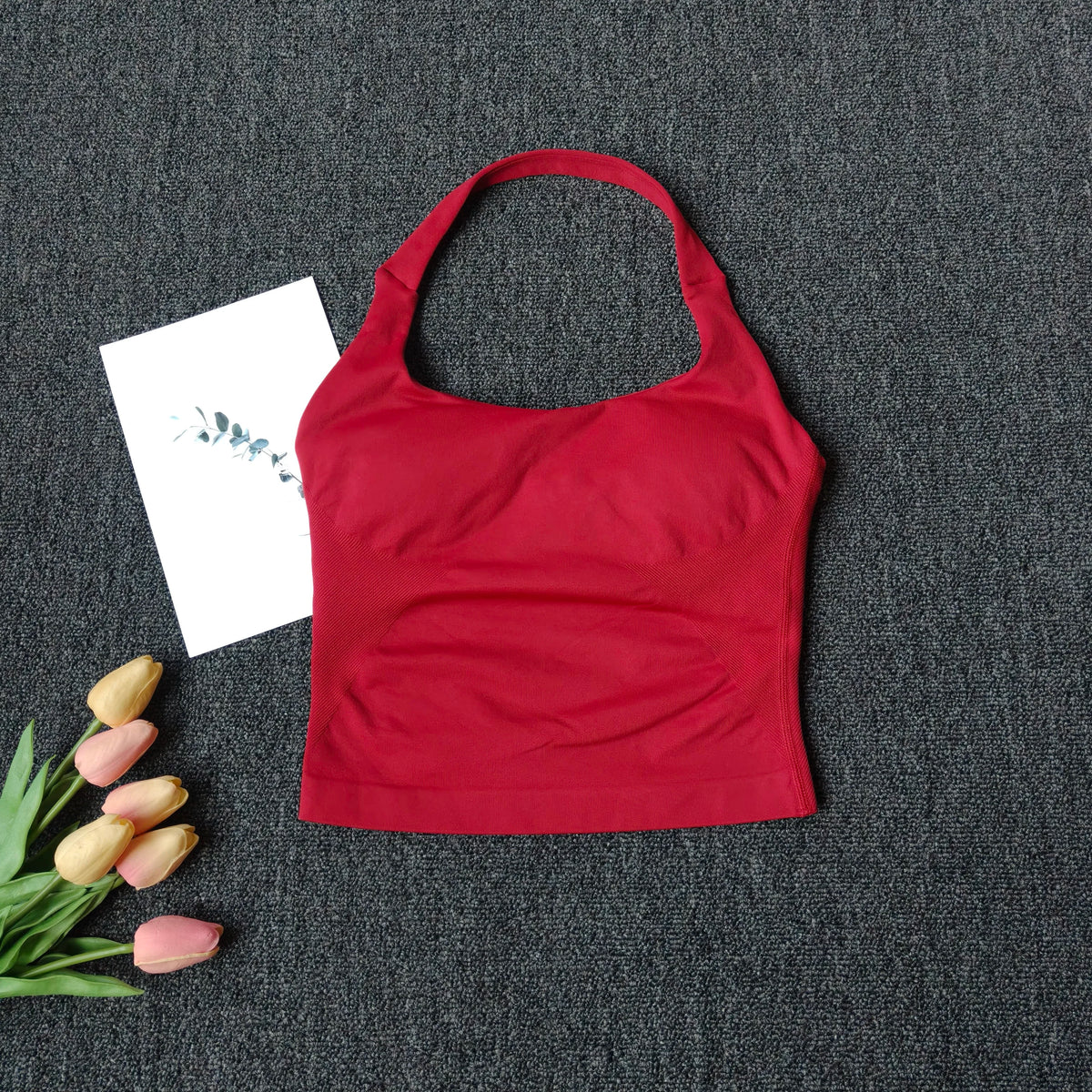 A red seamless yoga and pilates sports bra laid on a dark gray fabric with some dried flowers nearby.