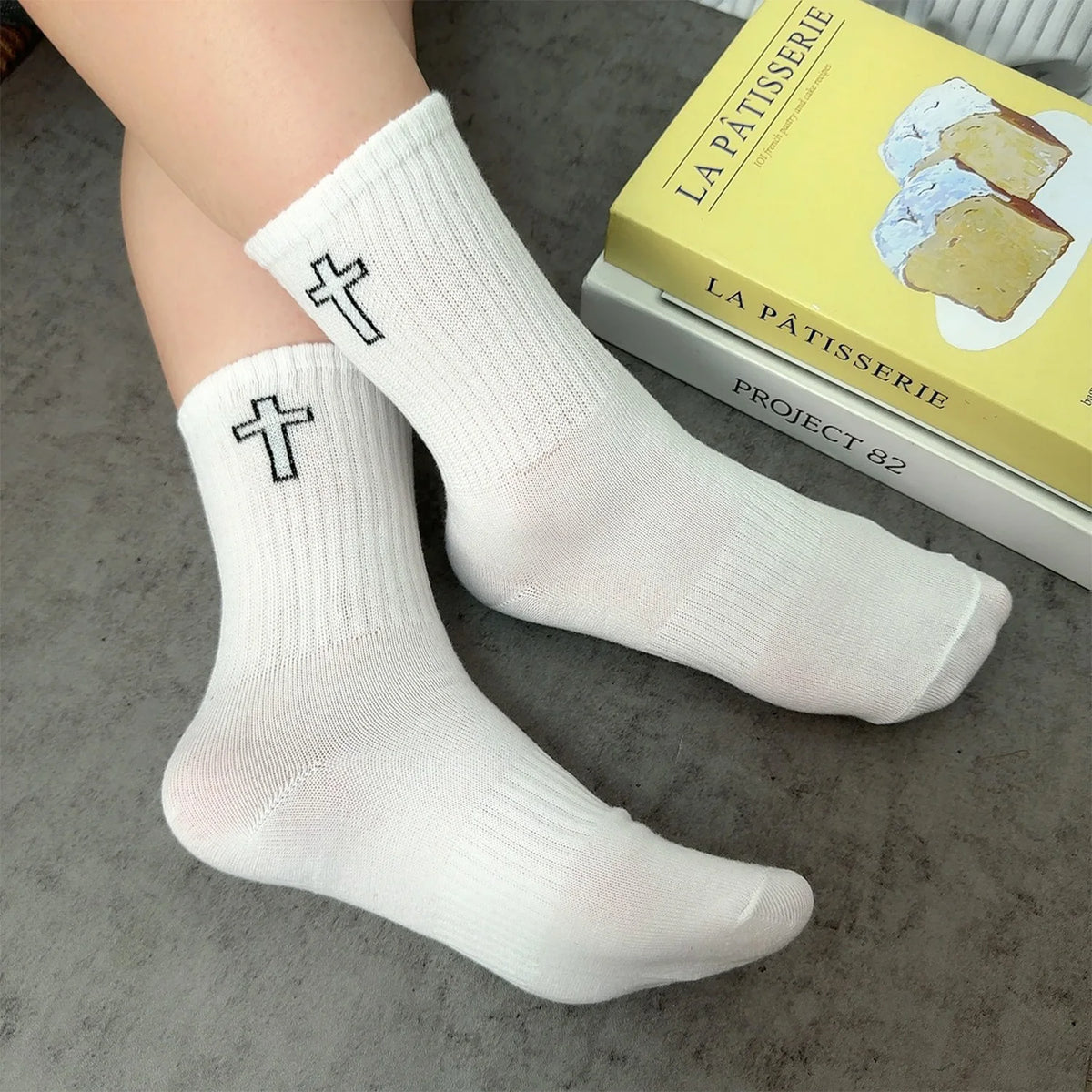 A pair of white crew socks with a cross design lying next to a box labeled La Pâtisserie Project 82