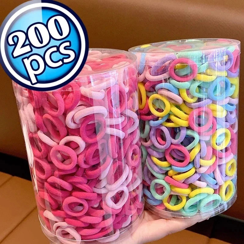 Eine Hand hält zwei klare Behälter mit bunten Nylon-Haargummis in verschiedenen Rosa-, Gelb- und Grüntönen.