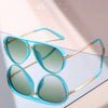A pair of classic gradient aviator sunglasses with light blue frames and green lenses resting on a white surface.