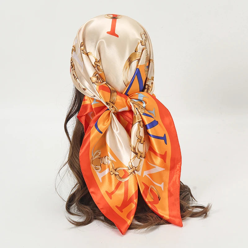 A satin orange scarf with gold embroidery featuring the letter I, worn around a dark hair.
