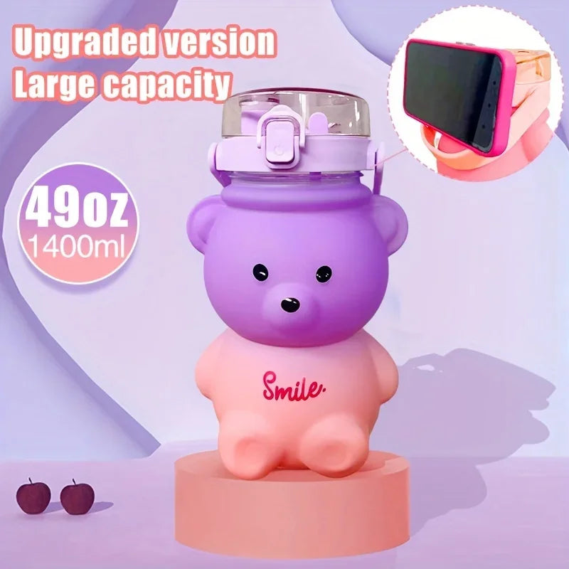 A purple bear-shaped water bottle with a straw and strap is displayed on a pink stand.