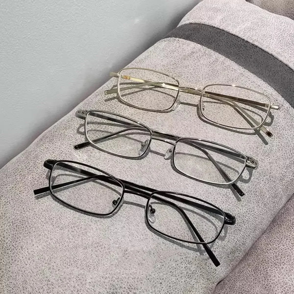 A collection of four eyeglasses with various styles and frames resting on a light gray textured surface.
