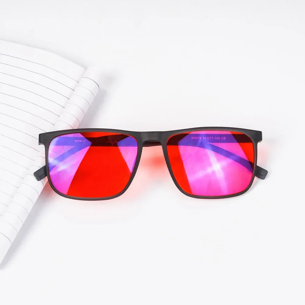 A pair of red tinted blue light blocking glasses resting on a white spiral notebook.