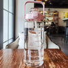 Una botella de agua transparente con tapa y pajita rosa sobre una mesa de madera.