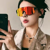 Eine Frau mit orange getönten Sport-Sonnenbrillen und goldfarbener Jacke, die ein Smartphone hält.
