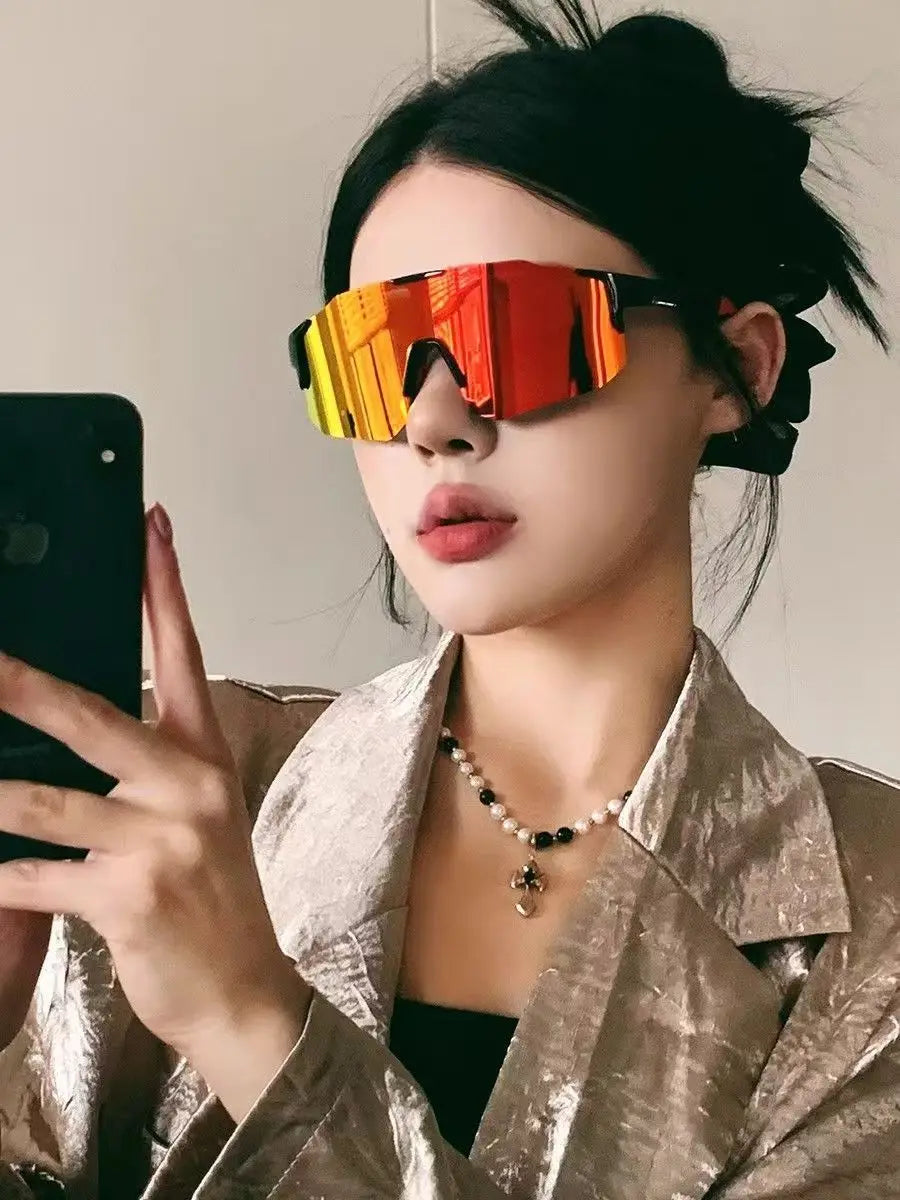 Eine Frau mit orange getönten Sport-Sonnenbrillen und goldfarbener Jacke, die ein Smartphone hält.
