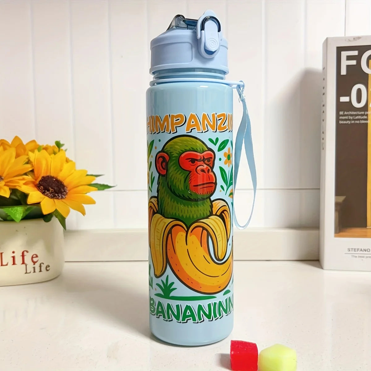 A light blue insulated sports water bottle shaped like a monkey holding a banana, sitting on a white surface.