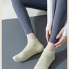 A pair of light green non-slip yoga socks worn by a person sitting on a gray mat.