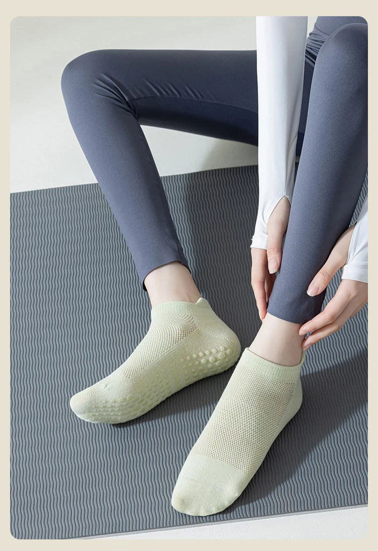 A pair of light green non-slip yoga socks worn by a person sitting on a gray mat.
