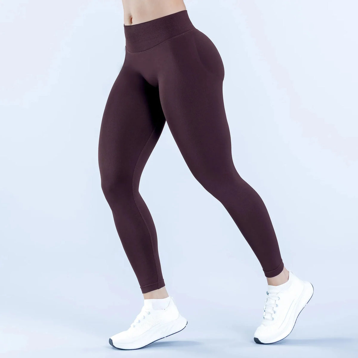 Model trägt dunkle Pflaumente, hoch taillierte, nahtlose Yoga-Leggings und weiße Sneaker.