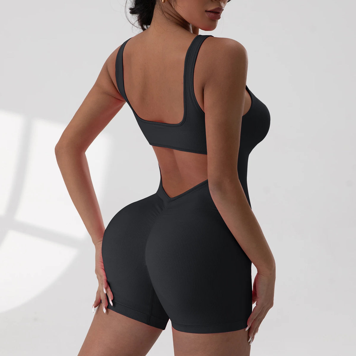 A woman models a black tie-dye sport jumpsuit from the back view.