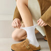 Gros plan d'une personne portant des chaussettes en tricot blanc et des mocassins en daim marron sous un manteau beige.