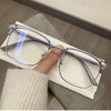 A pair of silver-framed retro square blue light blocking eyeglasses resting on a white paper next to a person's hand.