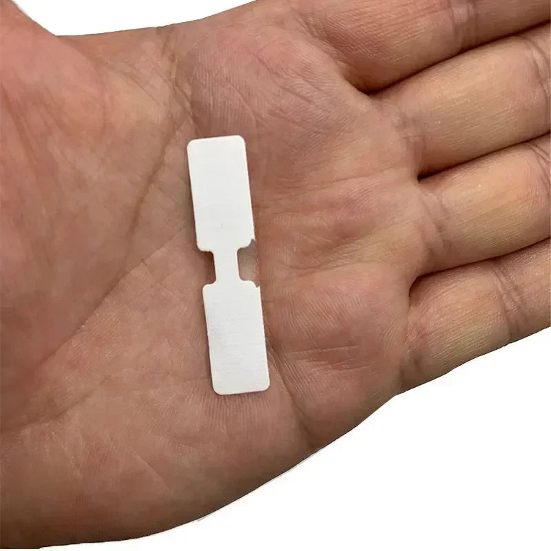 A hand holds a white adhesive wound patch, showing its size and shape.
