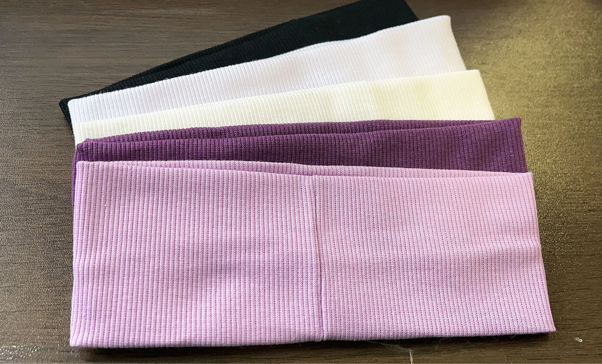 A stack of five elastic hairbands in various colors including black, white, beige, purple, and pink.