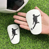 A hand holds a white ergonomic mouse featuring a black silhouette of a soccer player in a dynamic pose, resting on green gras