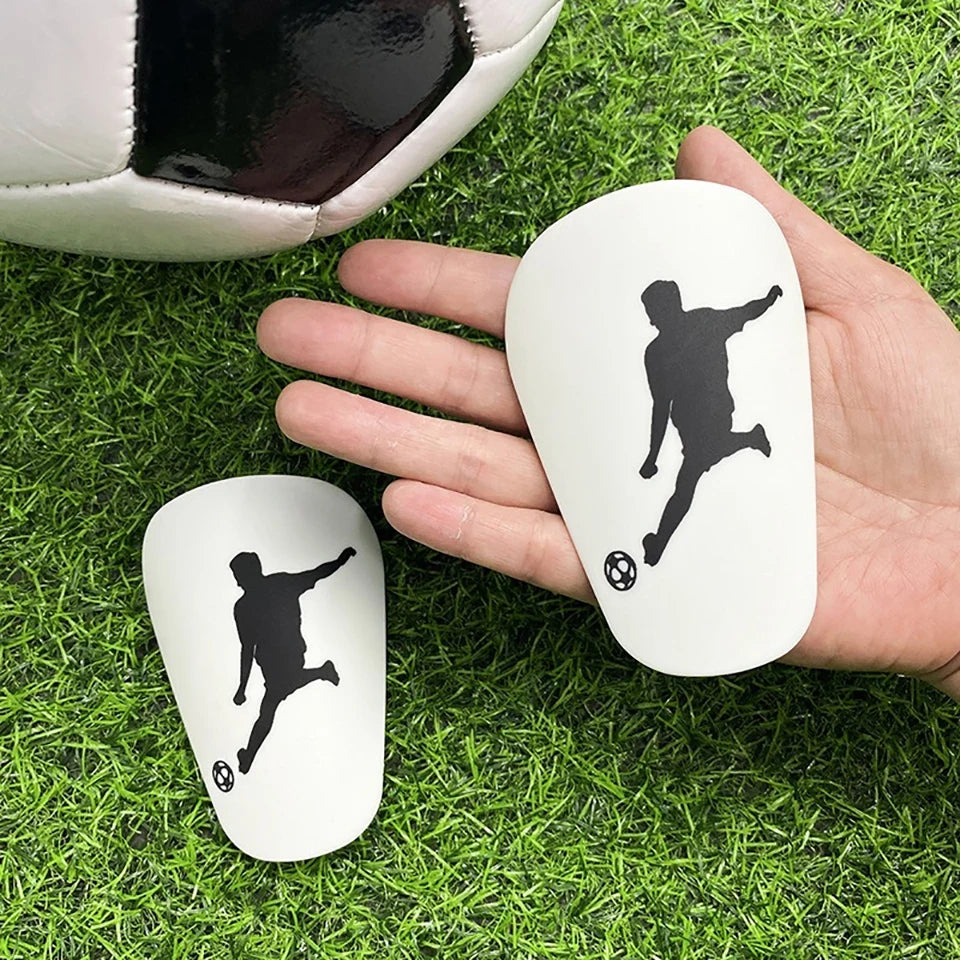 A hand holds a white ergonomic mouse featuring a black silhouette of a soccer player in a dynamic pose, resting on green gras