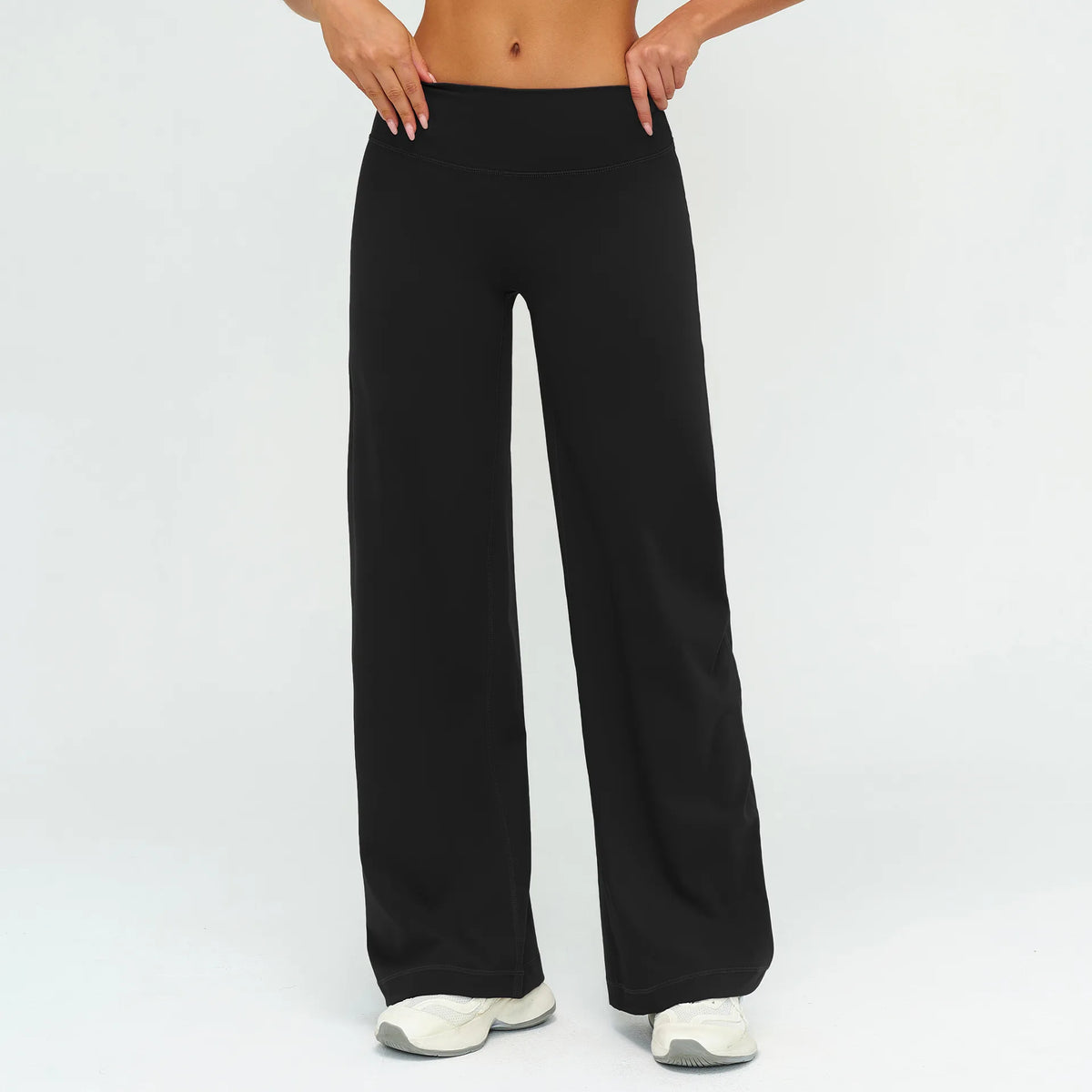 A woman wearing black high-waist flared yoga pants and white sneakers.