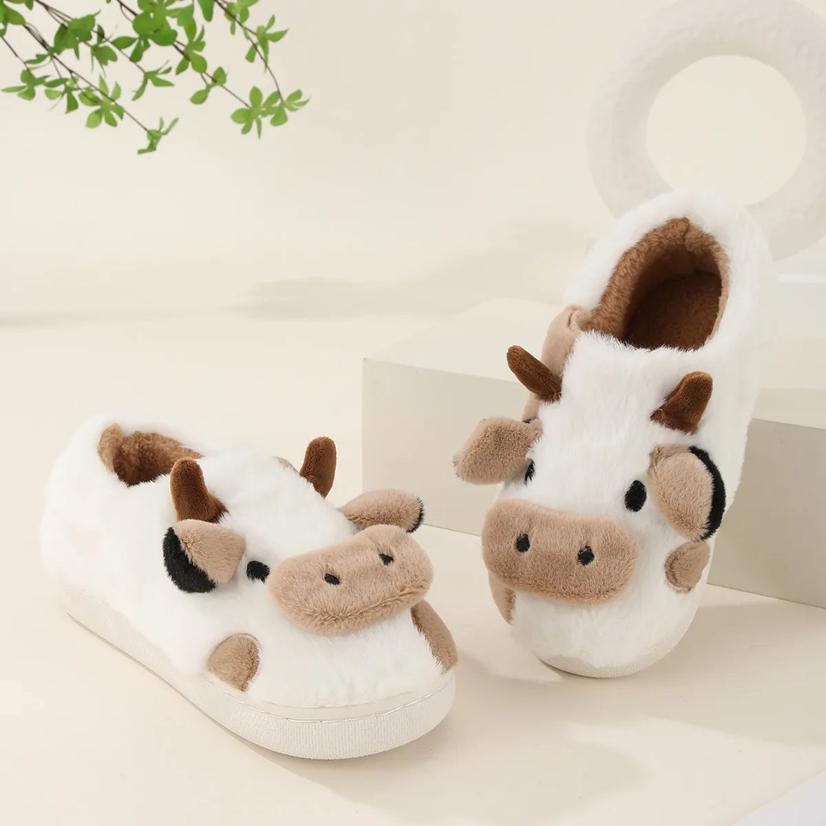 White cartoon cow winter home slippers with brown accents resting on a light surface.
