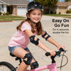A smiling girl wearing a black helmet and protective gear riding a pink bicycle.