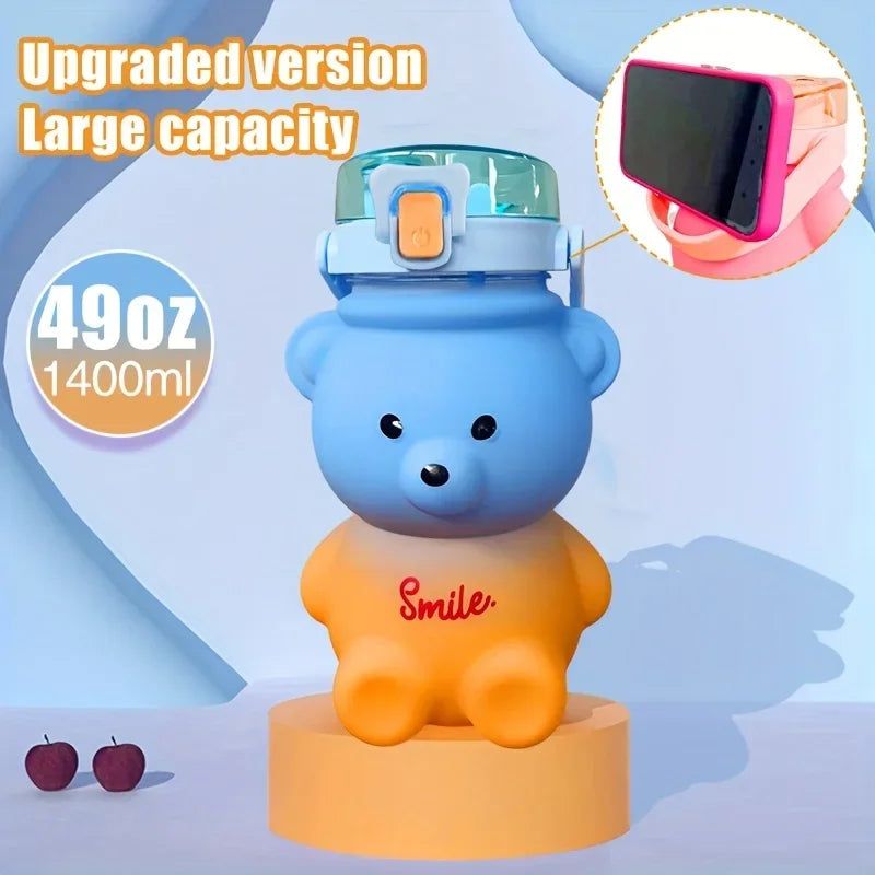 A blue bear-shaped water bottle with a straw and strap is displayed on an orange stand.