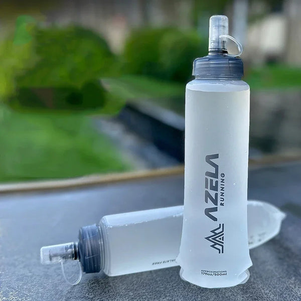 A clear silicone water bottle with a pump dispenser is shown against a blurred green outdoor background.