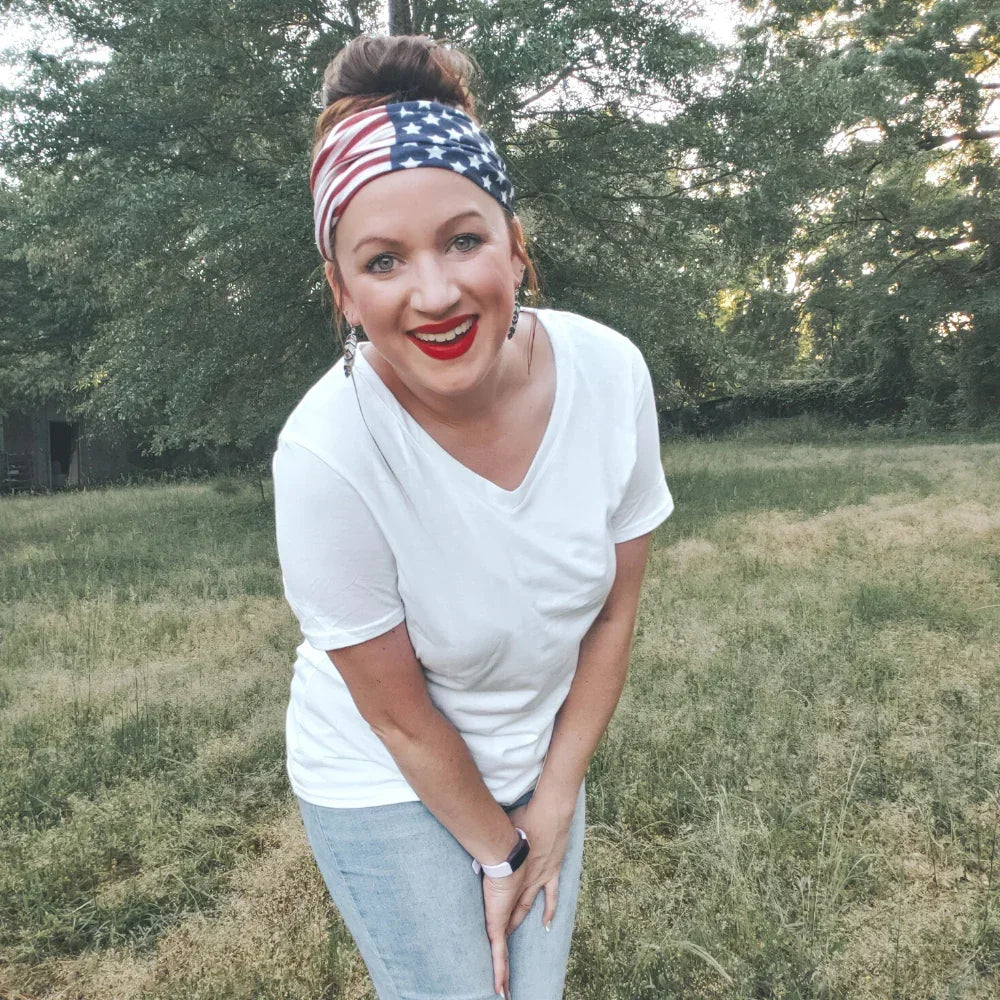 A woman wearing a USA flag bandana head wrap and a white t-shirt standing outdoors.