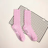 Pair of pink knitted mid-calf yoga and pilates socks laid on a black grid mat.