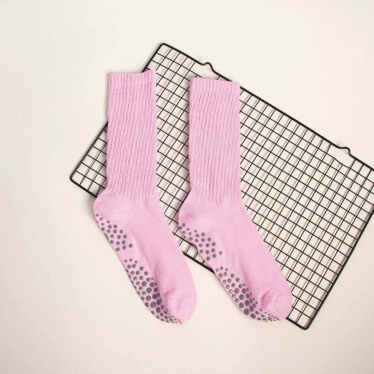 Pair of pink knitted mid-calf yoga and pilates socks laid on a black grid mat.