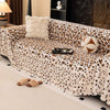 A plush leopard print sofa cover blanket draped over a sofa, featuring a white fluffy pillow and decorative accents.