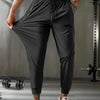 A muscular man models black breathable casual jogger pants in a gym setting.