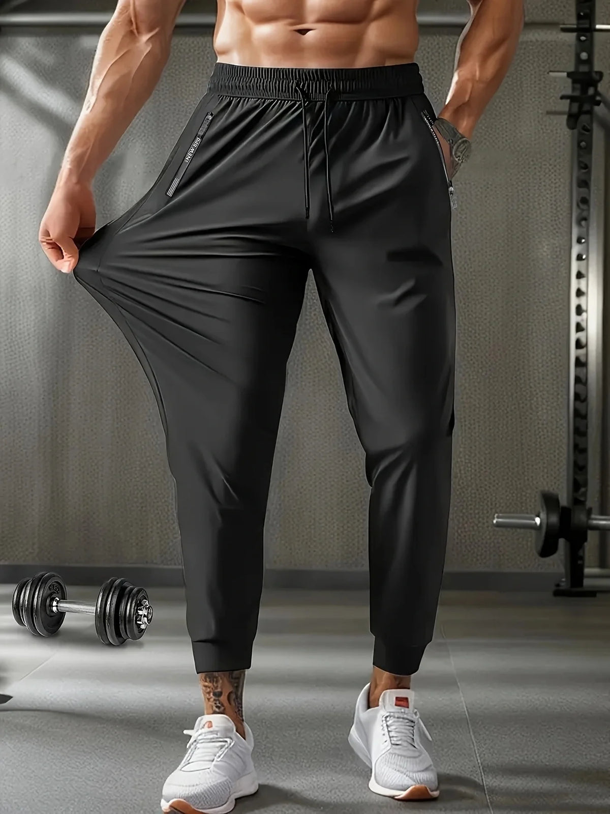 A muscular man models black breathable casual jogger pants in a gym setting.