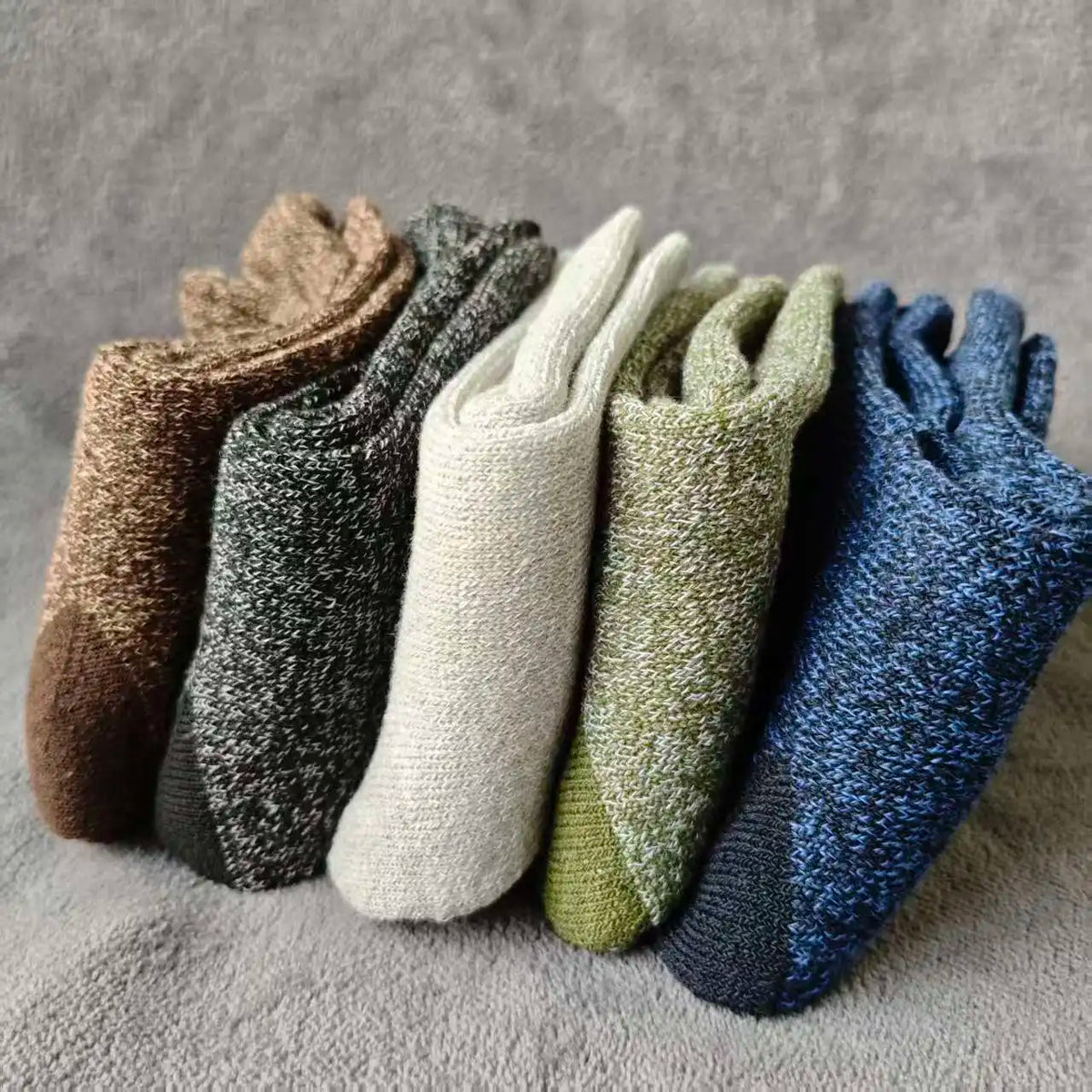 A pack of four merino wool hiking socks in various earthy and cool tones laid out on a gray surface.