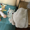 A folded soft coral fleece face towel with gray stripes rests on a teal pillow next to a stuffed animal.