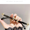A hand holds a pair of frameless photochromic prescription glasses with gold accents against a dark lace garment.