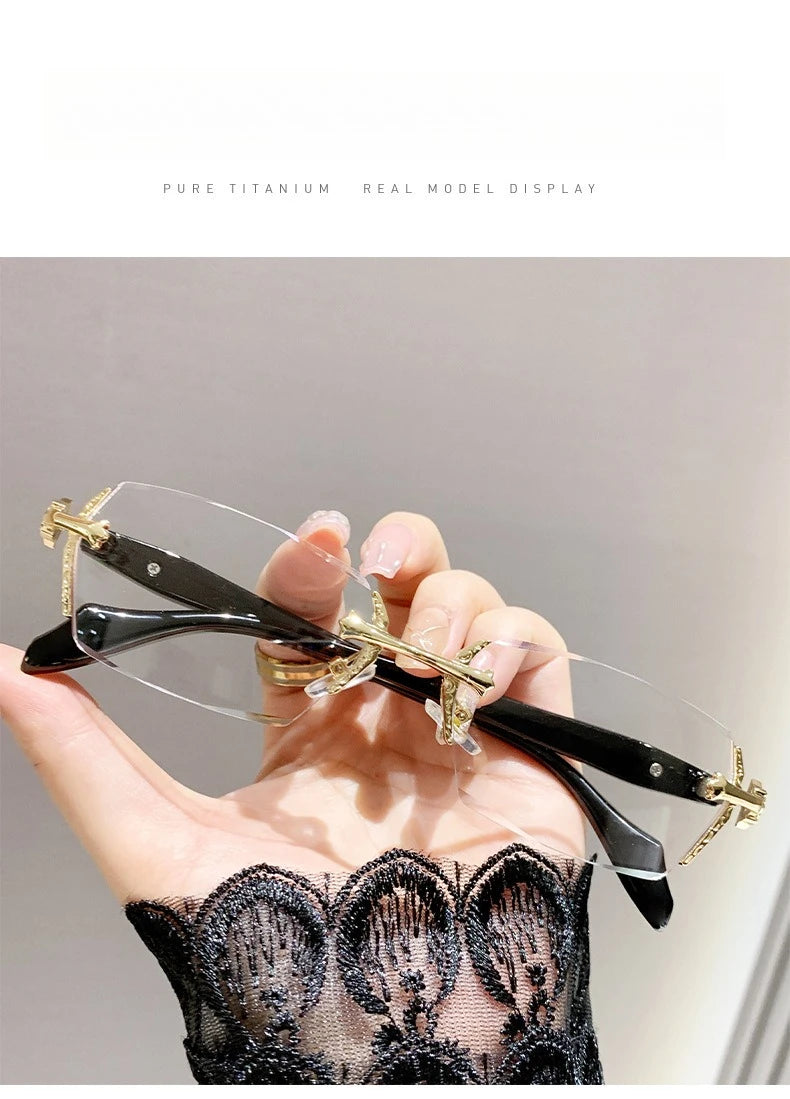 A hand holds a pair of frameless photochromic prescription glasses with gold accents against a dark lace garment.