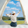 A person is sitting inside a white tent looking out through an arched opening at a scenic landscape.