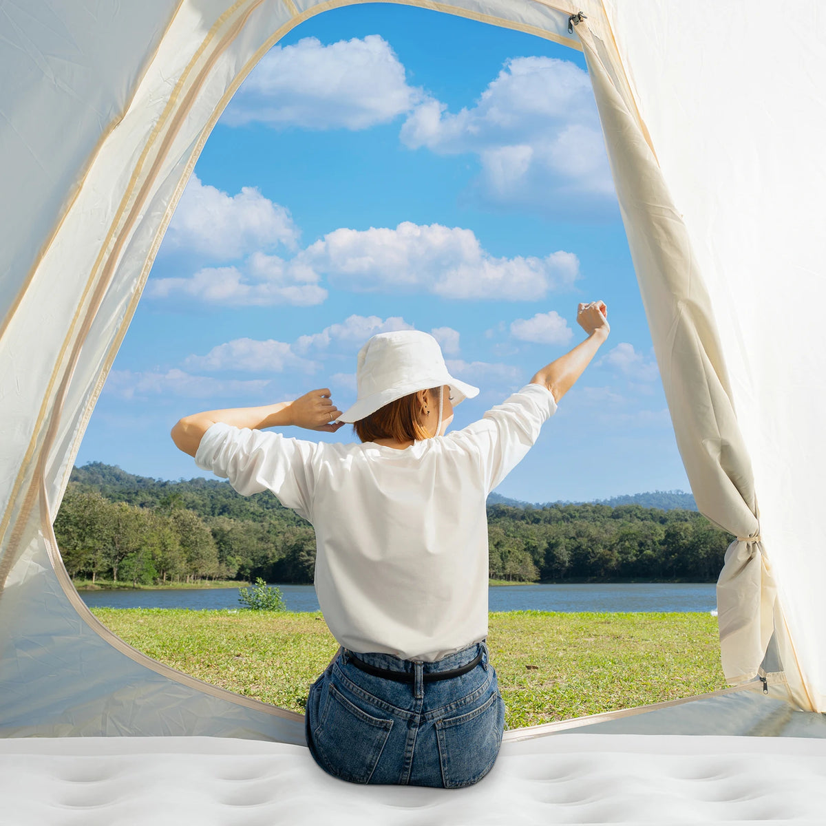 A person is sitting inside a white tent looking out through an arched opening at a scenic landscape.