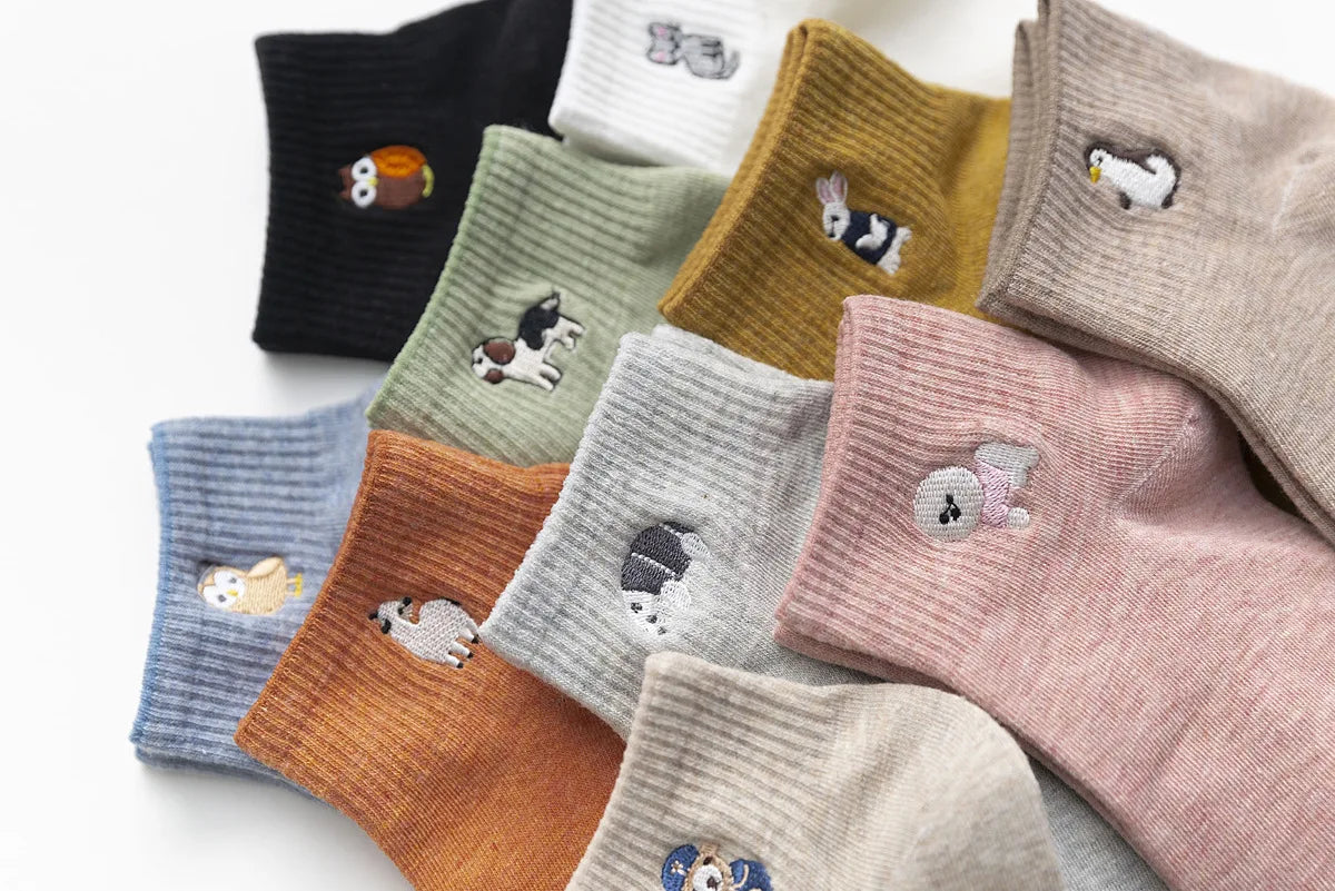 A collection of embroidered cotton socks in various muted colors including black, olive green, beige, and pink.