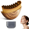 A golden face brush with brown bristles rests in a wooden storage case next to a gray silicone tool.