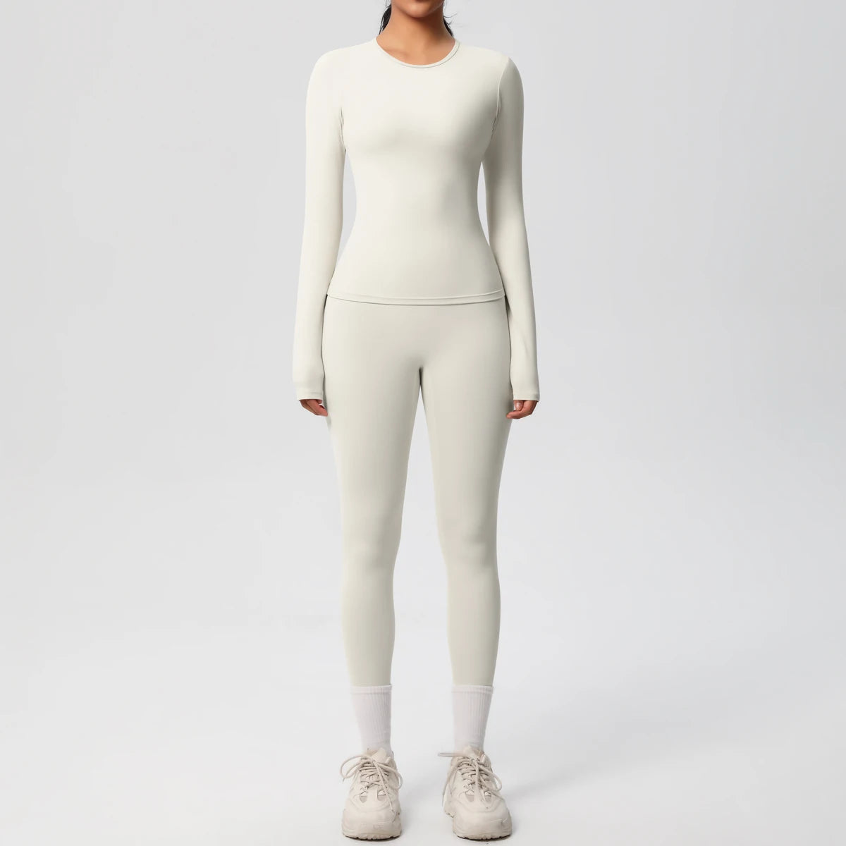 A woman wearing a long-sleeved cream performance yoga set with matching leggings and white socks.