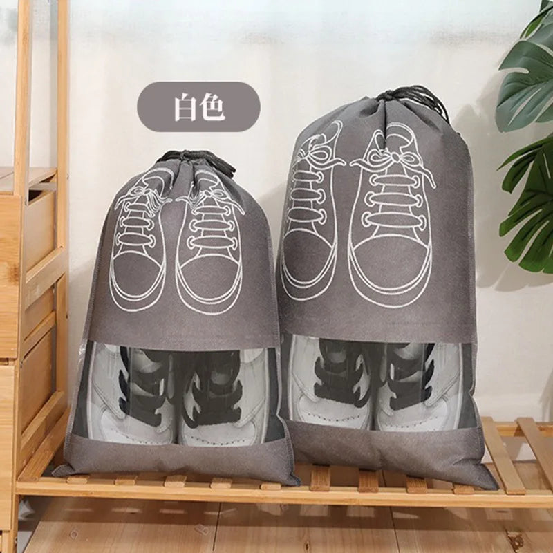 A pair of grey reusable non-woven shoe storage bags with white laces are displayed on a wooden shelf.