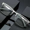 A pair of silver-framed reading glasses with clear lenses resting on a dark surface.