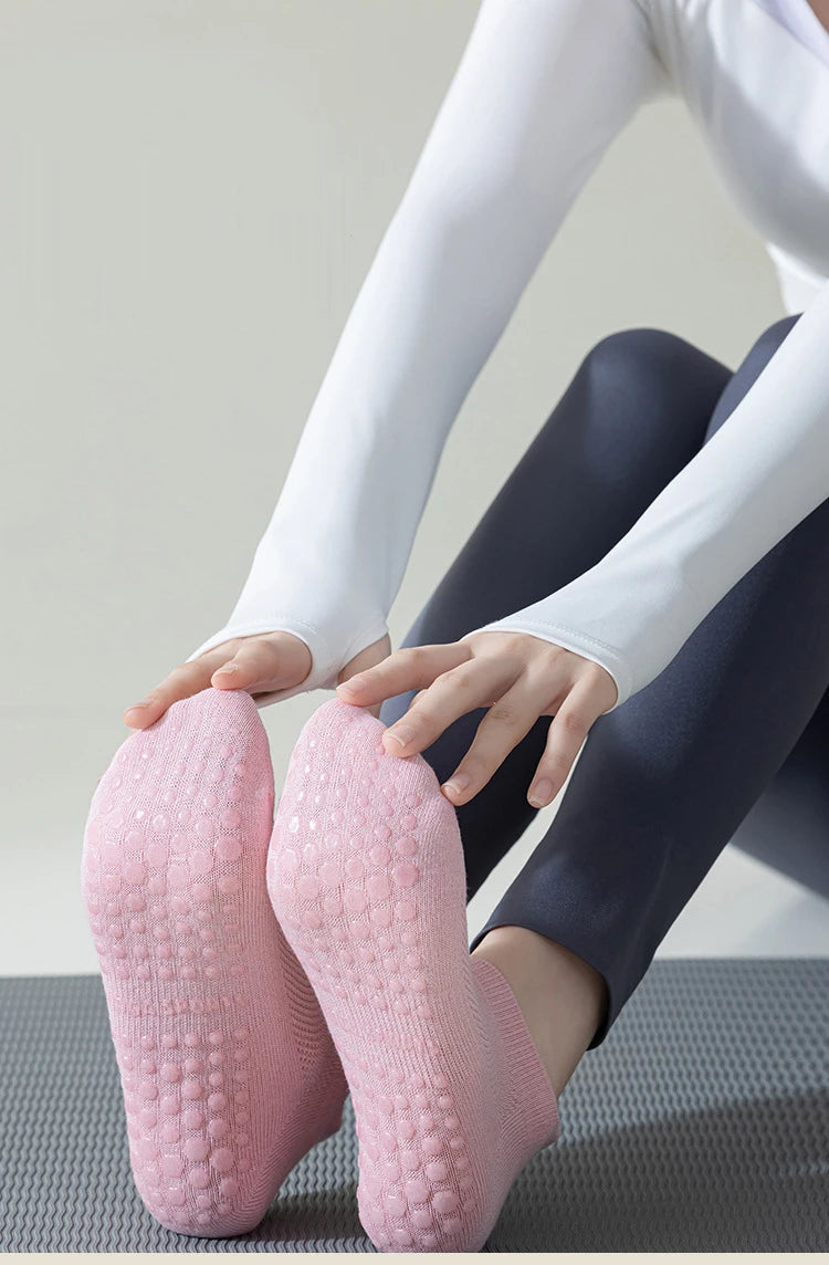 A pair of pink non-slip yoga socks being worn by a person in a gray setting.