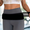 A woman wearing gray athletic wear is using a black adjustable pelvic support hip belt for lower back and SI joint relief.