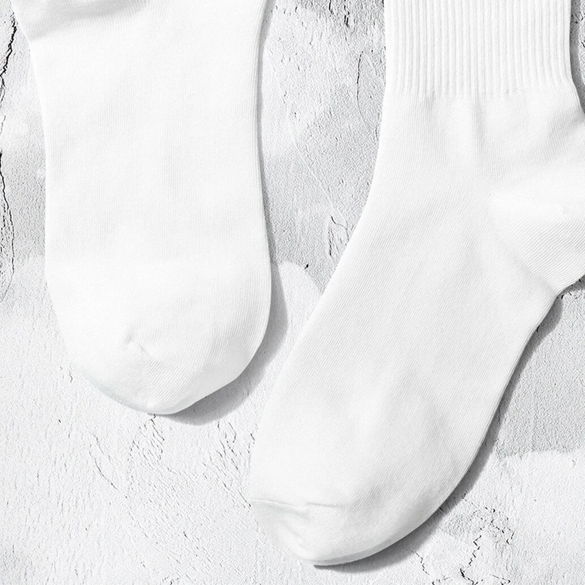 A pair of white crew socks with subtle lettering lying on a light textured surface.