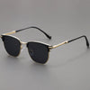 Black sunglasses with a gold-toned metal frame and black arms resting on a gray surface.