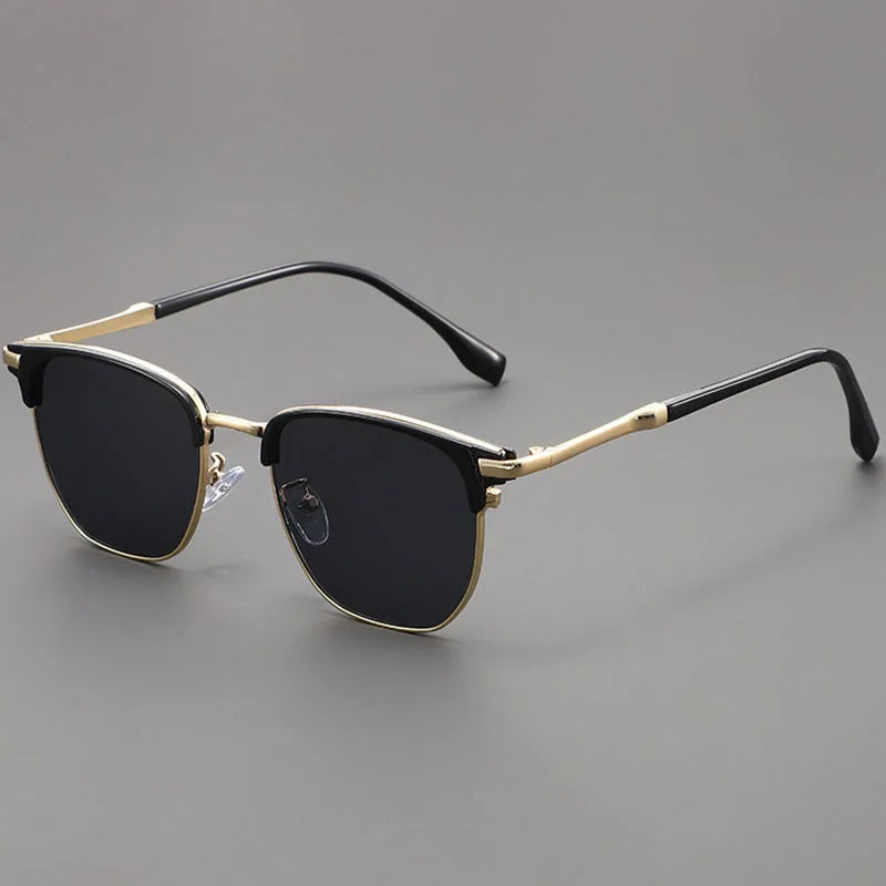 Black sunglasses with a gold-toned metal frame and black arms resting on a gray surface.