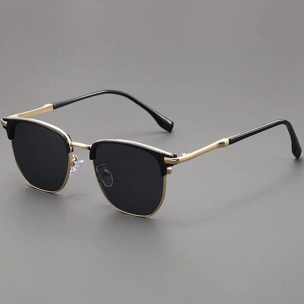 Black sunglasses with a gold-toned metal frame and black arms resting on a gray surface.
